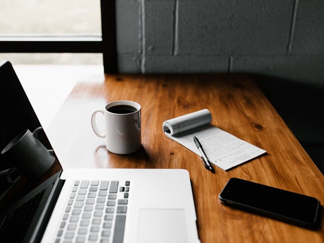 A desk with a laptop, notebook and coffee